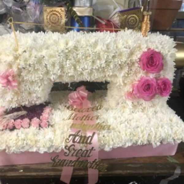 White floral arrangement with pink roses and a pink ribbon on a pink base