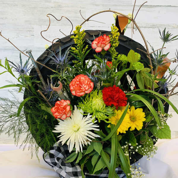 Mixed flower arrangement in a tire-shaped container with a checkered ribbon