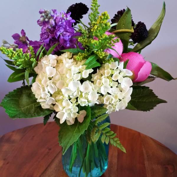 Mixed bouquet of white hydrangeas, purple blooms, and pink tulips in a blue vase