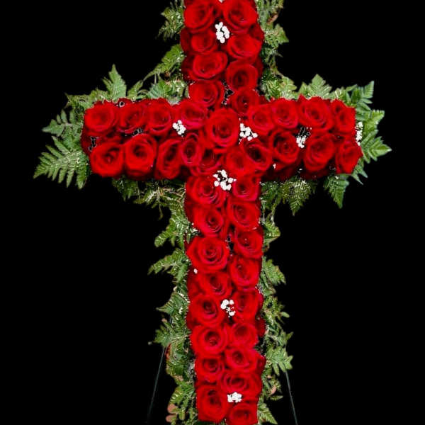 Cross-shaped arrangement of red roses with greenery on a black background