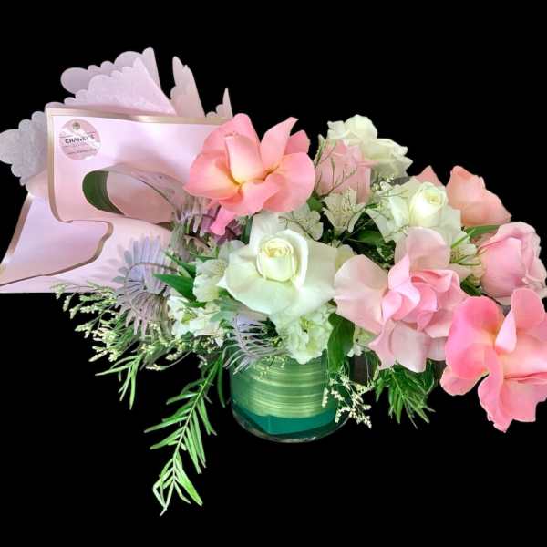 Pink and white floral arrangement in a green glass vase with a card