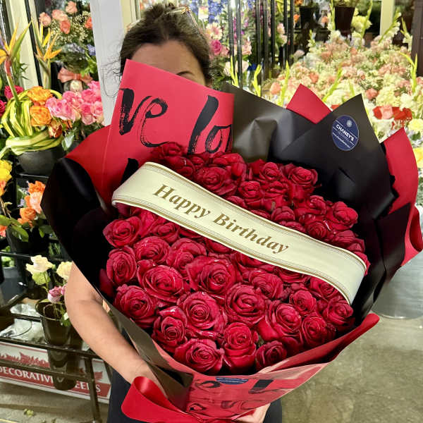 Large bouquet of red roses wrapped in black and red paper with a birthday ribbon