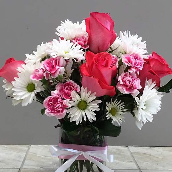 Pink roses and white daisies in a glass vase with a ribbon