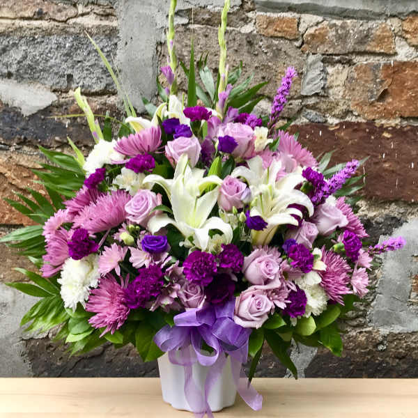 Purple and white floral arrangement in a white vase with a lavender ribbon