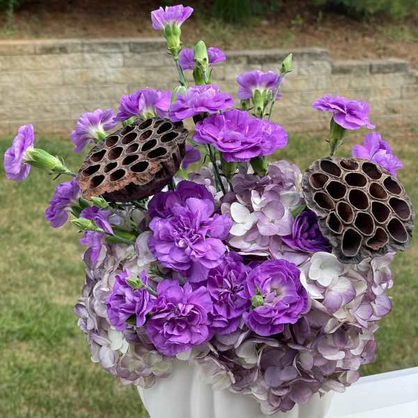 Purple flowers arranged in a white vase with dried seed pods
