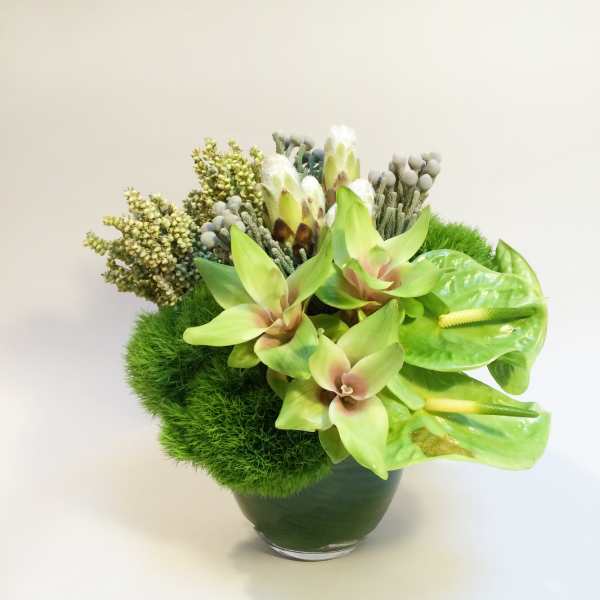 Green floral arrangement in a glass vase with anthuriums and textured blooms