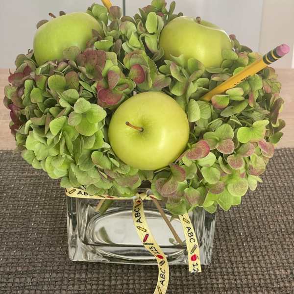 Green hydrangea arrangement with apples and pencils in a glass vase