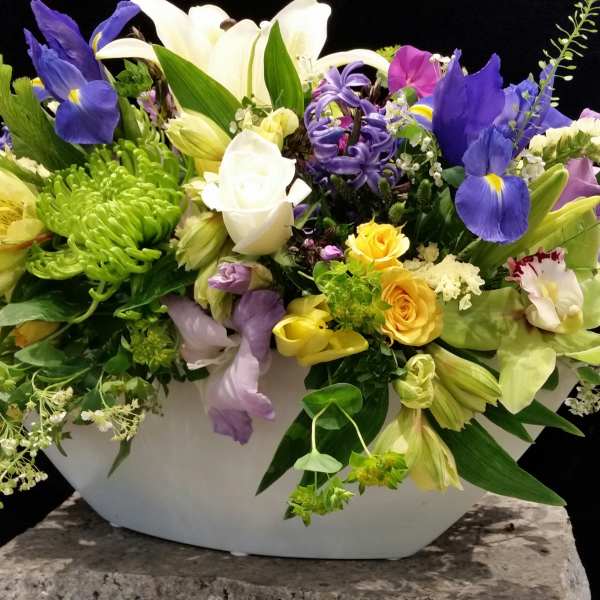 Mixed bouquet in a white container with blue, yellow, and purple flowers