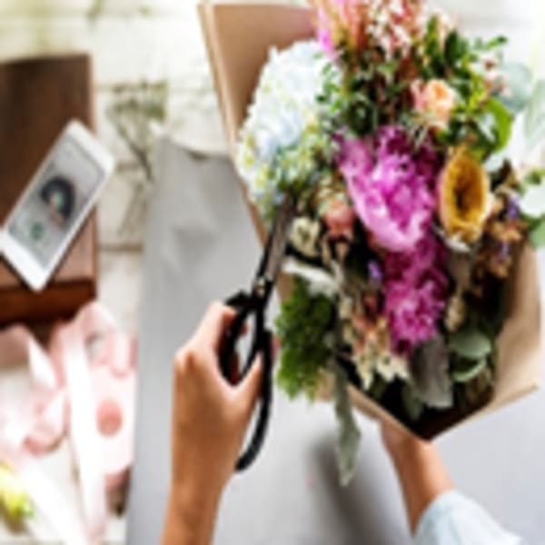 Hand holding scissors near a colorful bouquet wrapped in paper