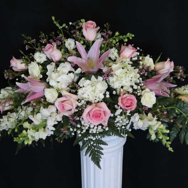 Pink roses and white flowers arranged in a white pedestal vase
