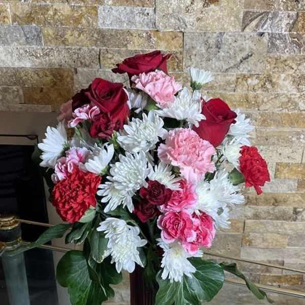 Bouquet of red roses, pink carnations, and white daisies in a red vase
