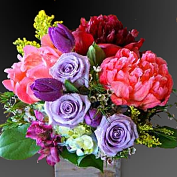 Mixed bouquet of pink, purple, and red flowers in a square glass vase