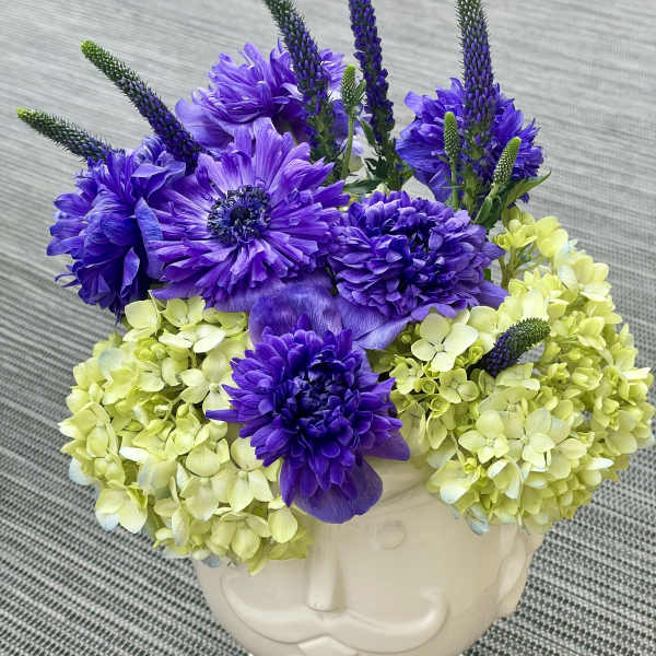 Purple flowers and pale green hydrangeas in a white face vase