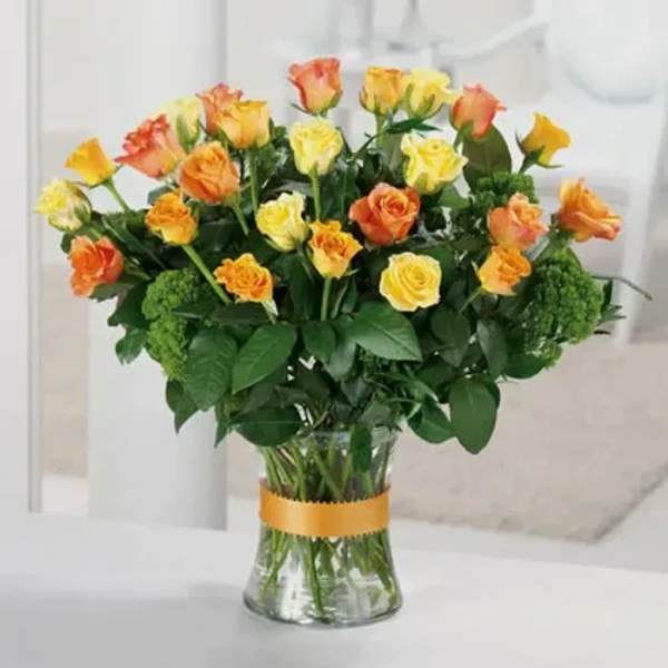 Bouquet of yellow and orange roses in a clear glass vase with an orange ribbon.