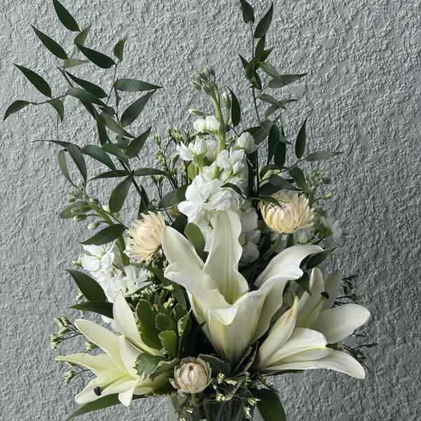 White lilies and pale blooms in a clear glass vase