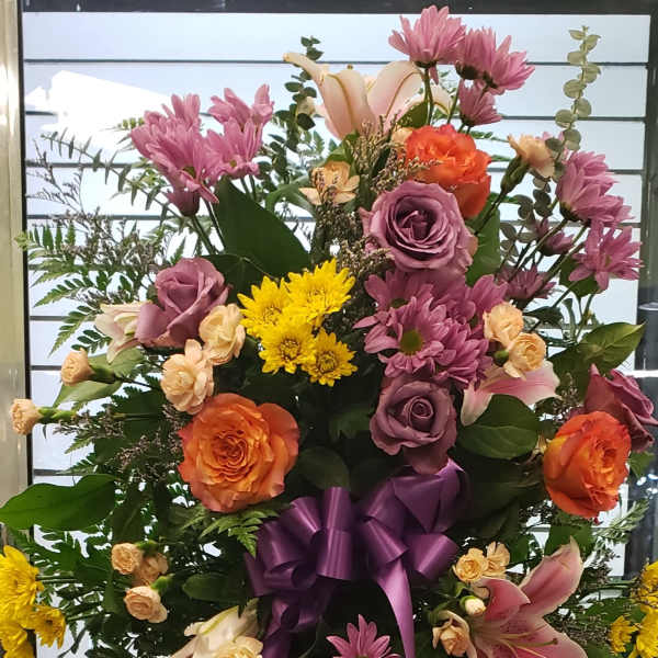 Large standing floral spray with roses, lilies, and chrysanthemums tied with a purple ribbon