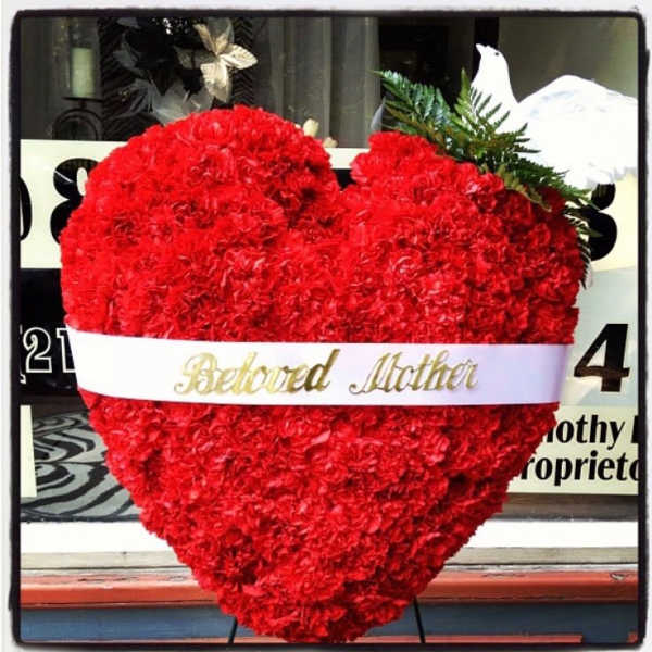 Heart-shaped red carnation arrangement with a white ribbon