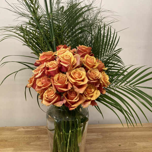 Orange roses arranged in a clear glass vase with tall palm fronds