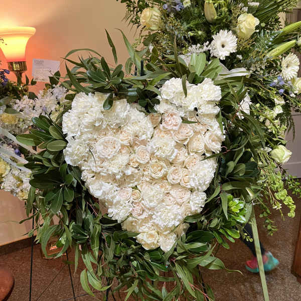 Heart-shaped white floral wreath on an easel with trailing greenery