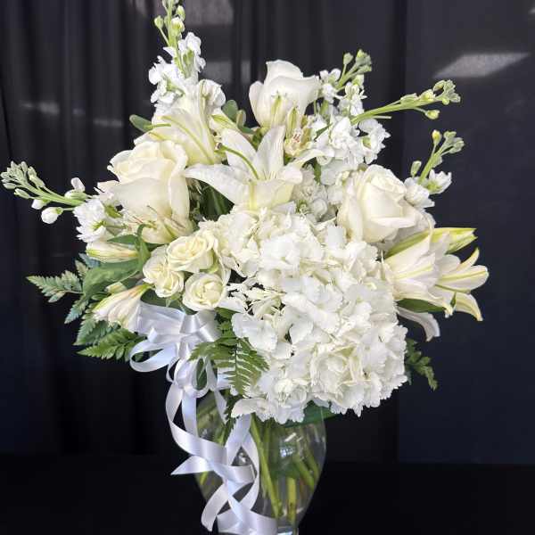 White floral arrangement in a clear glass vase with a white ribbon