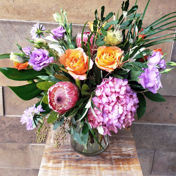 Mixed bouquet with orange roses, pink hydrangea, and purple blooms in a glass vase