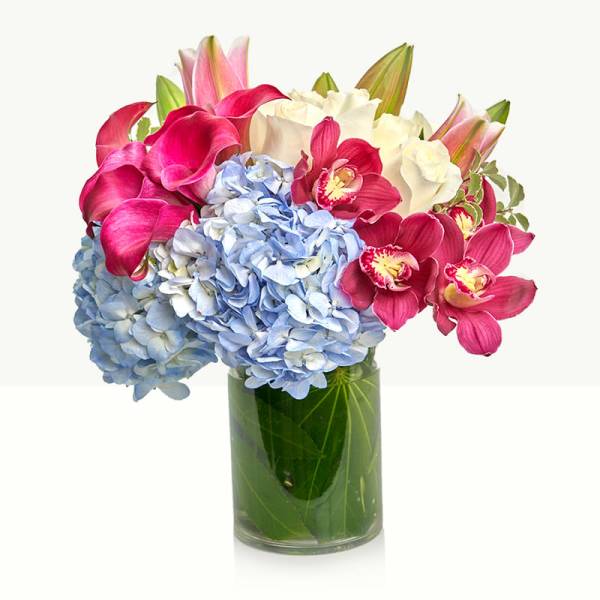 Bouquet of blue hydrangeas, pink calla lilies, and orchids in a glass vase