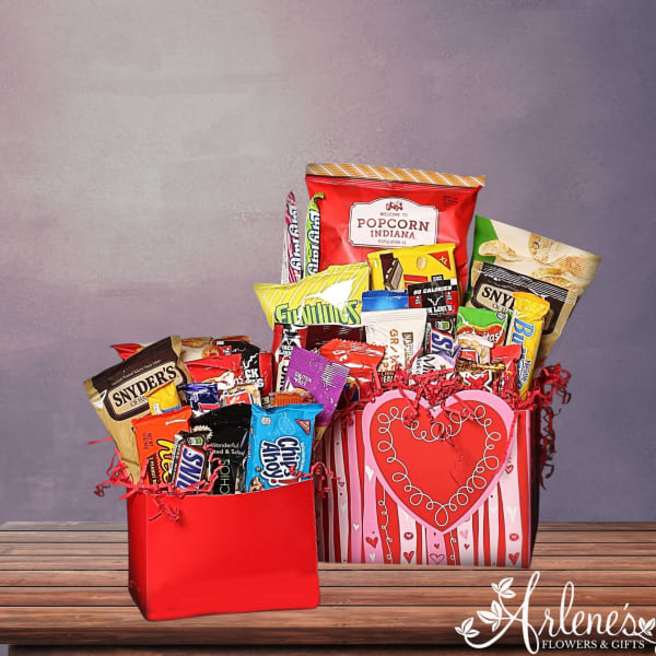 Two red gift boxes filled with assorted chips, candy bars, and popcorn on a wooden tabletop.
