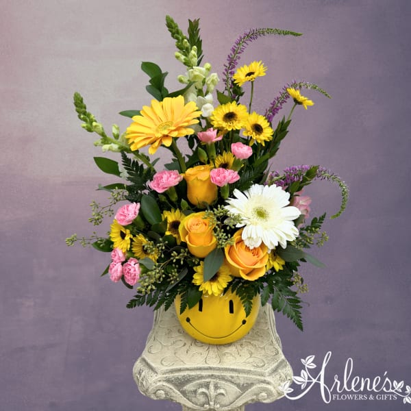 Mixed yellow, pink, and white flowers in a smiley-face pot