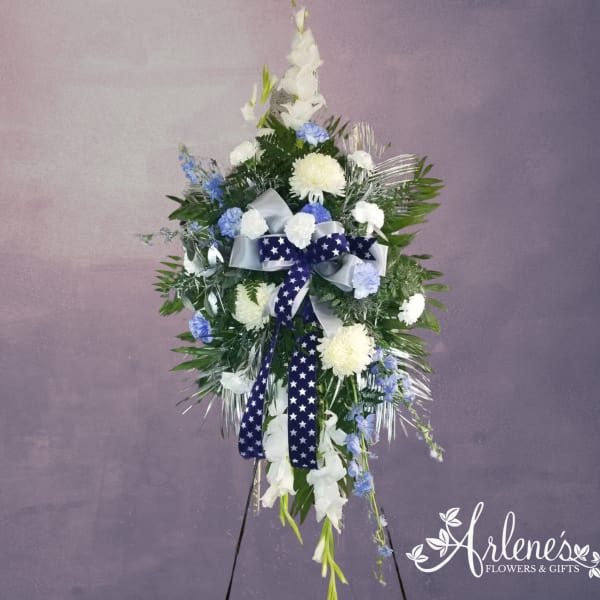Tall standing spray of white and blue flowers with star-patterned ribbon on an easel stand