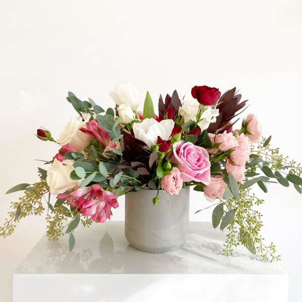 Mixed pink, white, and red flowers arranged in a gray vase