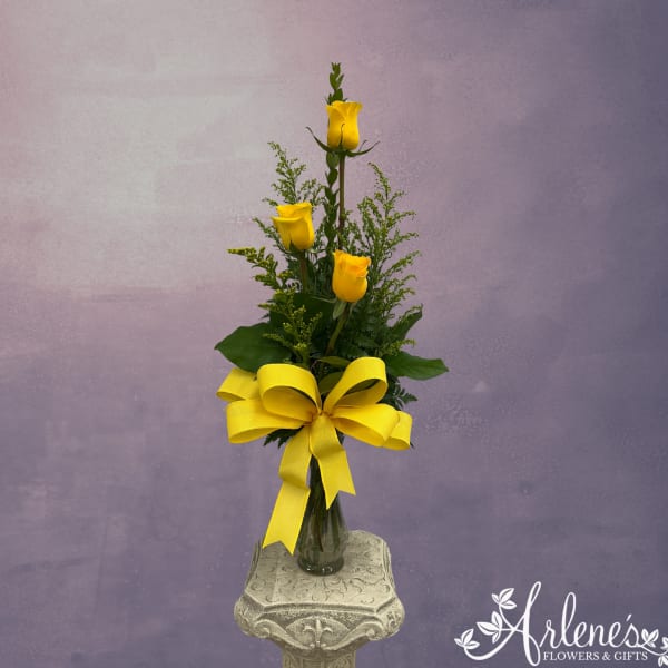 Tall arrangement of yellow roses in a glass vase with a large yellow bow