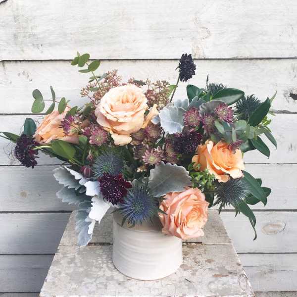 Peach roses and thistle in a white vase