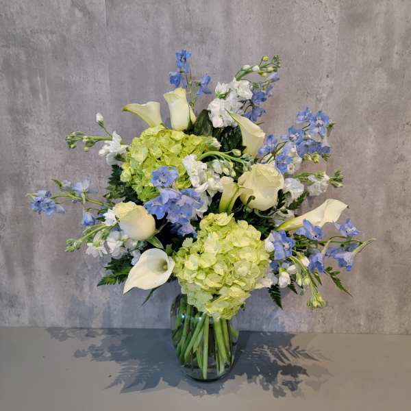 Blue and white flowers with pale green hydrangeas in a glass vase