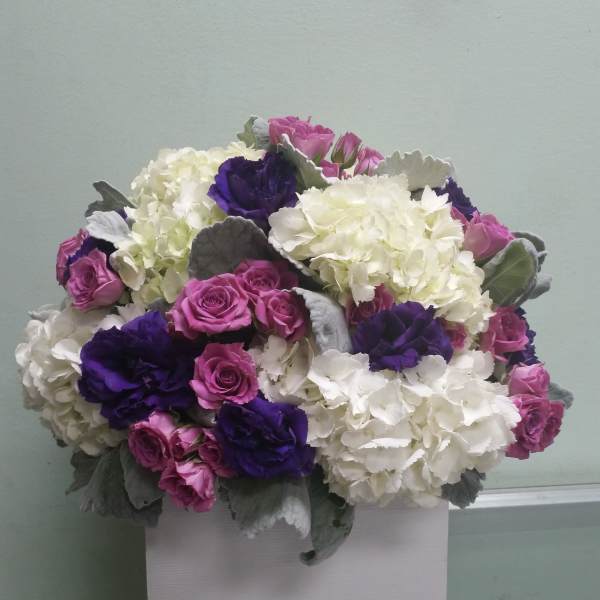 Bouquet of pink roses, white hydrangeas, and purple blooms in a white box