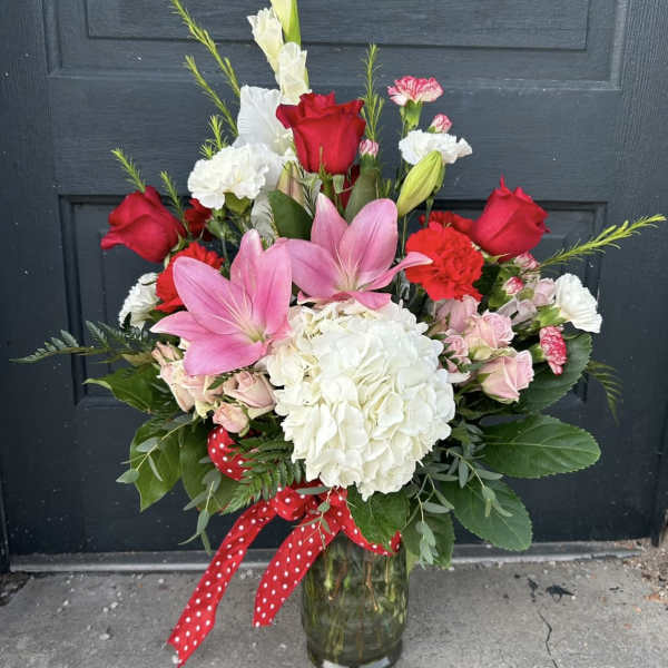 Bouquet of pink lilies, red roses, and white hydrangea in a glass vase