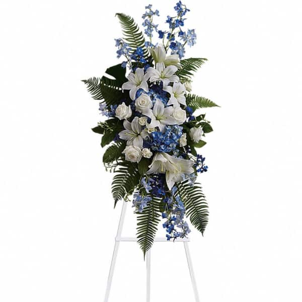 Tall standing spray of white lilies and roses with blue flowers on a white easel