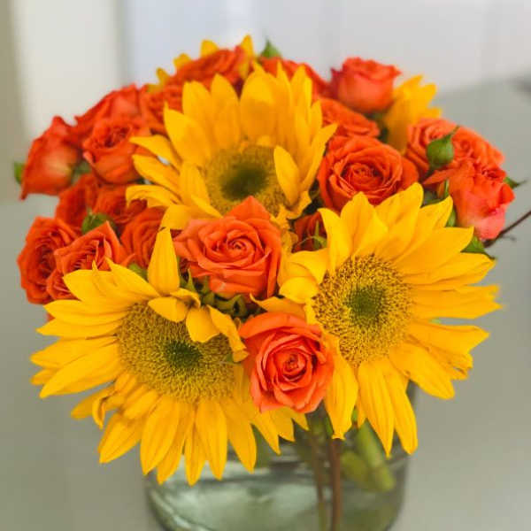 Sunflowers and orange roses in a clear glass vase