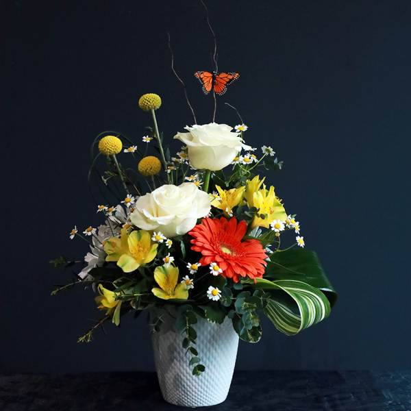 Mixed flower arrangement in a white vase with a butterfly accent