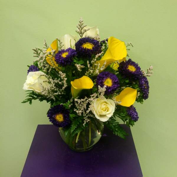 Bouquet of purple daisies, yellow calla lilies, and white roses in a glass vase