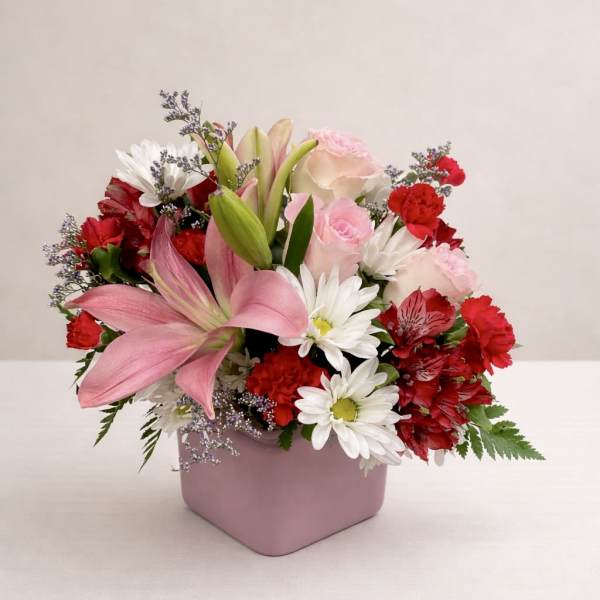 Pink lilies, roses, and daisies arranged in a pink square vase