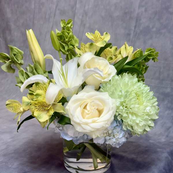 White roses, lilies, and green chrysanthemums in a clear glass vase