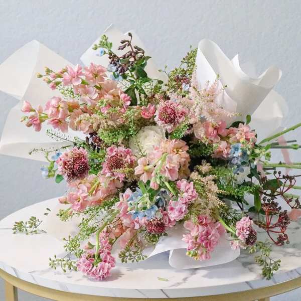 Loose bouquet of pink and blue flowers wrapped in white paper