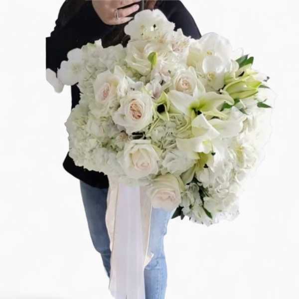 Large hand-tied bouquet of white roses, lilies, hydrangeas, and orchids with long white ribbon tails