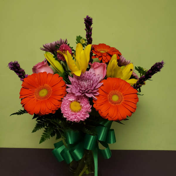 Bright mixed bouquet with gerbera daisies, lilies, and chrysanthemums in a glass vase