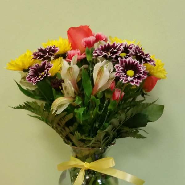Mixed bouquet of colorful flowers in a glass vase with a yellow ribbon