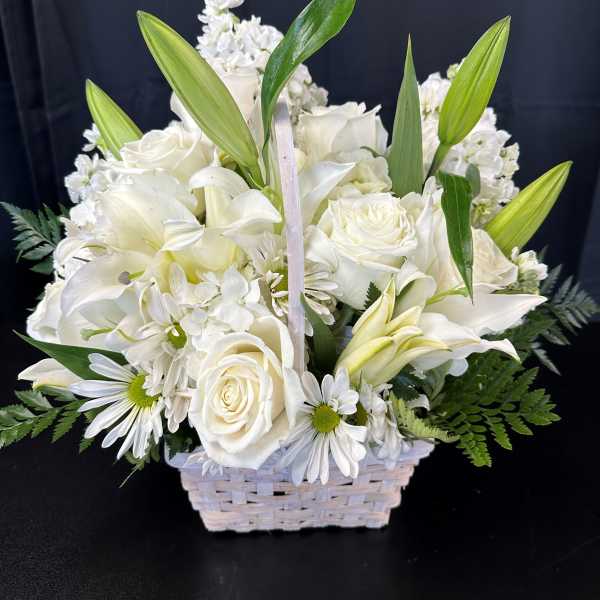 White floral arrangement in a woven basket with lilies and roses