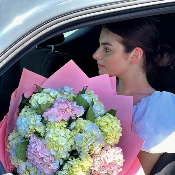 Woman holding a large bouquet of pastel hydrangeas in pink wrapping