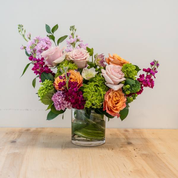 Mixed bouquet of pink, orange, and green flowers in a glass vase
