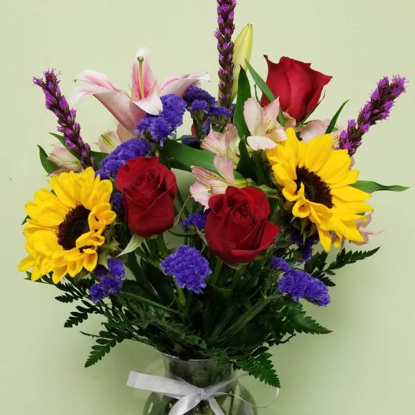 Bouquet of red roses, sunflowers, and pink lilies in a glass vase