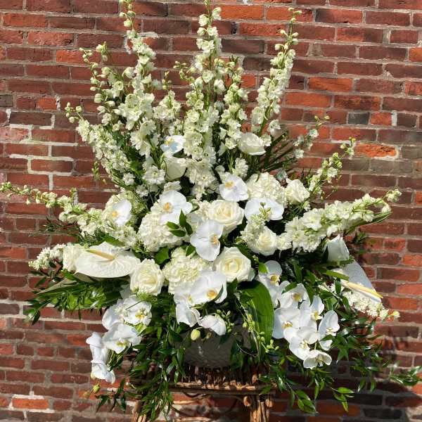 Large white floral arrangement with orchids and roses in a basket